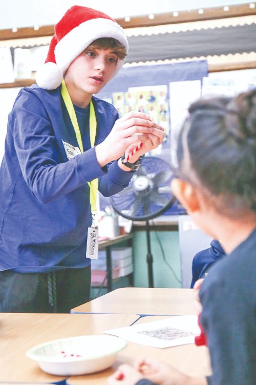 volunteer helping students make beaded candy canes